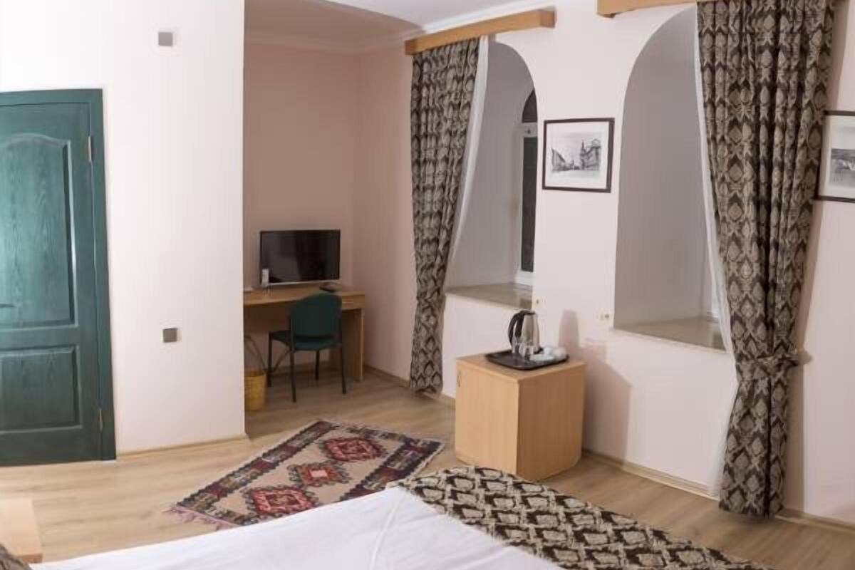 Une chambre à coucher comprenant un lit, un bureau, une chaise, une télévision et une petite table avec une bouilloire.