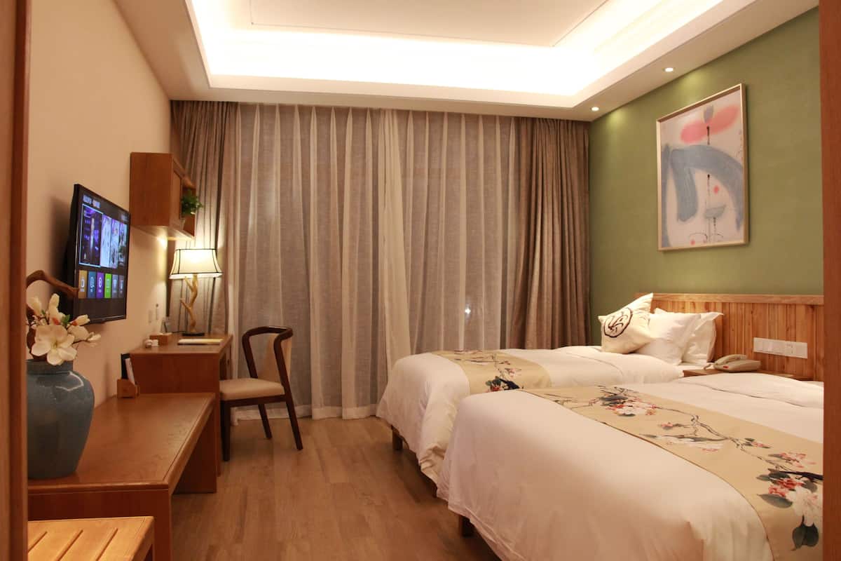 Habitación de hotel con dos camas, un escritorio con silla, un televisor y un cuadro en la pared.