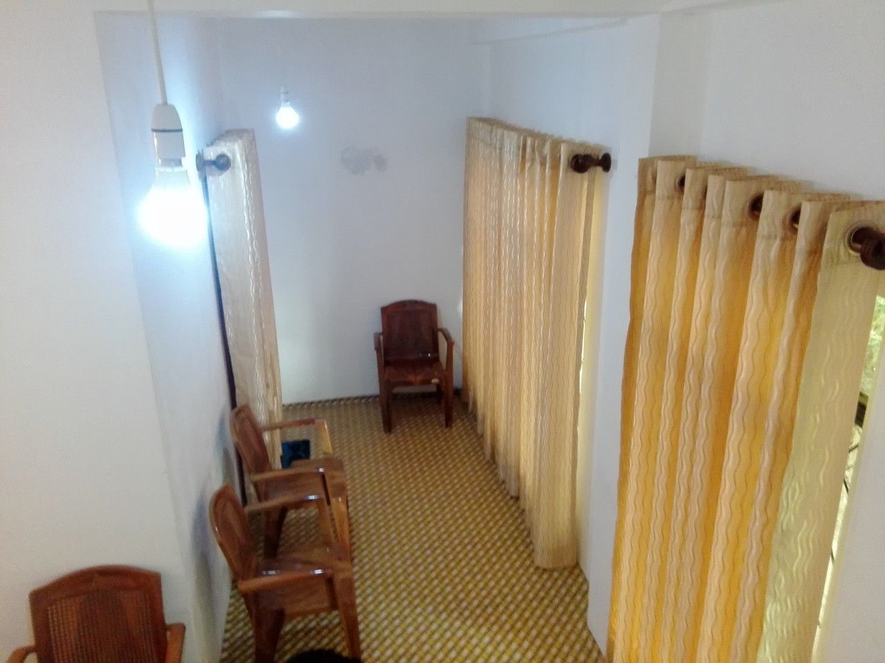Um quarto com carpete estampado, cadeiras e mesa de madeira, e uma cortina.