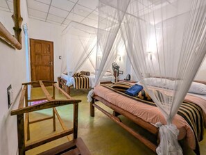 Een kamer met een bed onder een klamboe, een houten bank en een deur.