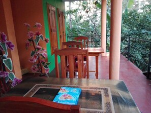 Een houten tafel en stoelen op een balkon met uitzicht op groen.