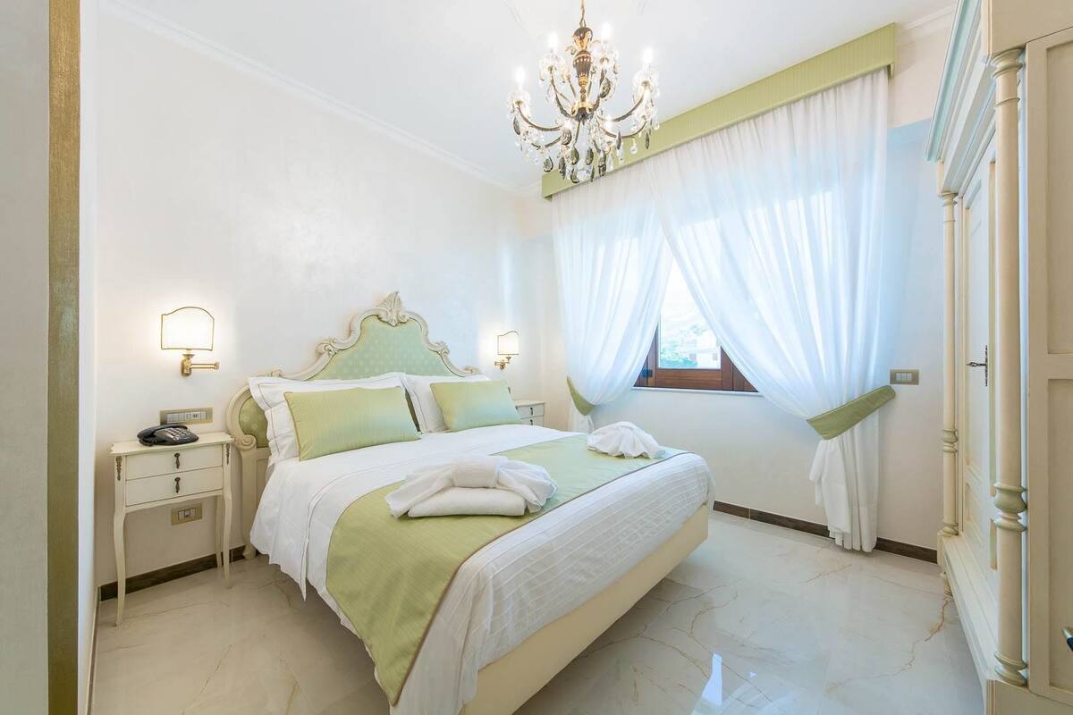 Une chambre à coucher avec un lit, des tables de chevet, un lustre et une fenêtre avec des rideaux.