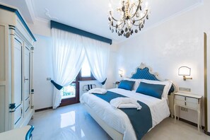 Une chambre à coucher avec un grand lit, un lustre, une table de chevet et une fenêtre avec des rideaux.