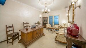 Une pièce spacieuse avec un bureau en bois, un globe terrestre et un ordinateur portable. On y trouve deux portes dotées de panneaux en verre bleu, un lustre et un miroir avec un cadre doré.