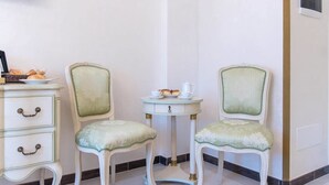 Une pièce comprenant deux chaises de style vintage, une petite table avec une théière et des tasses, et une commode blanche à tiroirs.