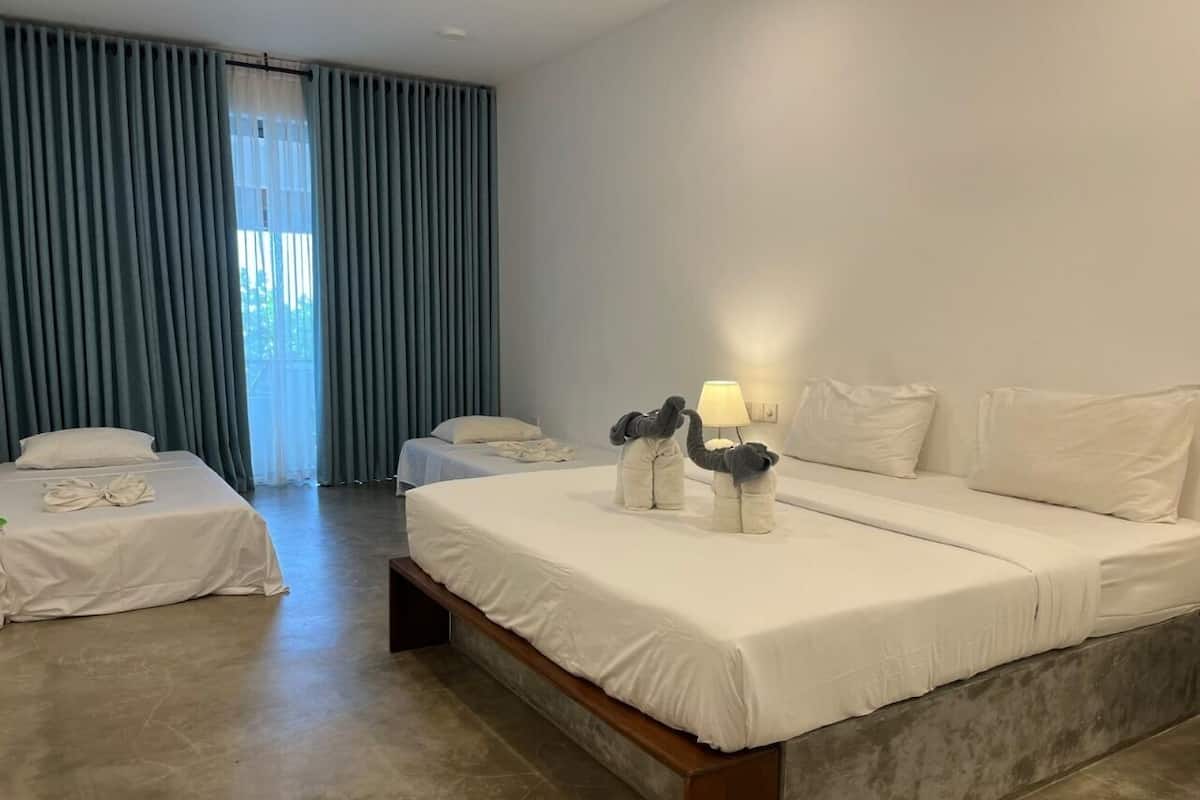 A hotel room with a large bed, a smaller bed, and a bench. There is a window with curtains and a lamp on the smaller bed.