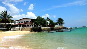 Un hôtel situé en bord de mer, doté d’un mur en pierre, de palmiers et d’une eau turquoise cristalline.