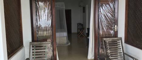 A doorway with two wooden chairs in front, a doormat, and a view into a room with a bed and a chair.
