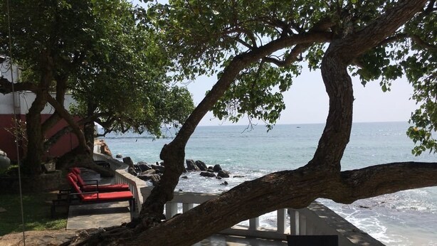 Une terrasse au bord de la plage, avec une chaise rouge, une table et une vue sur l’océan.