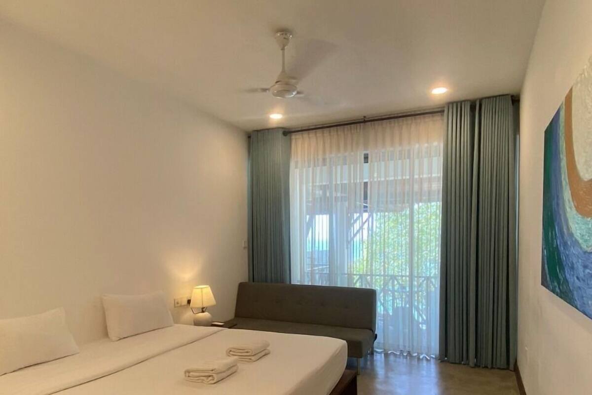 A hotel room with a large bed, a sofa, a ceiling fan, and a painting on the wall.