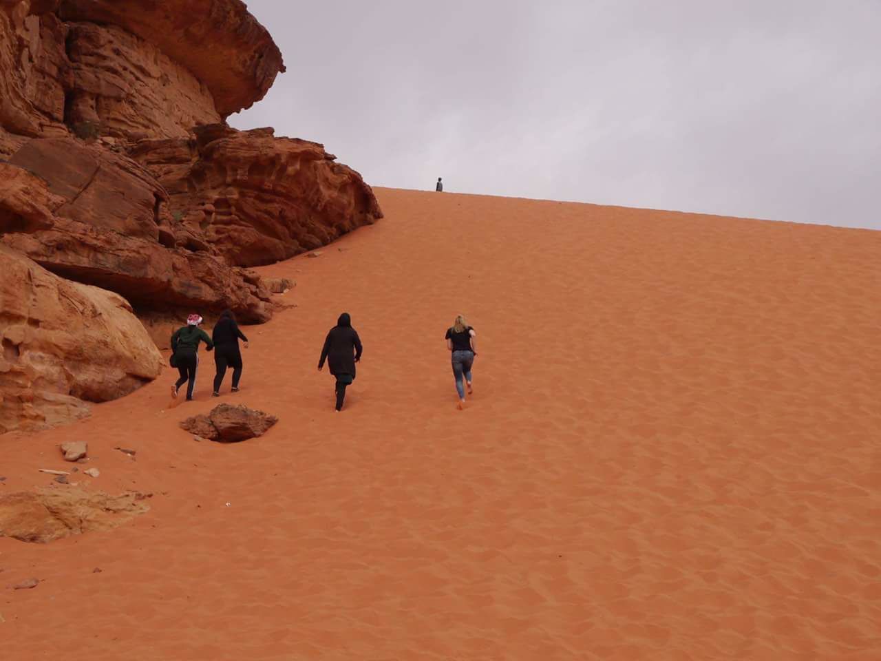 A group of people walking on a sandy slope with red rock formations.