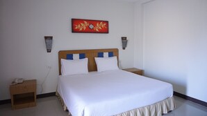 A hotel room with a large bed, a wooden headboard, two bedside tables, a wall-mounted artwork, and a plain white wall. - UD Residence (Udon Thani)