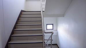 A staircase with a metal handrail, white walls, and a small window at the top. - UD Residence (Udon Thani)