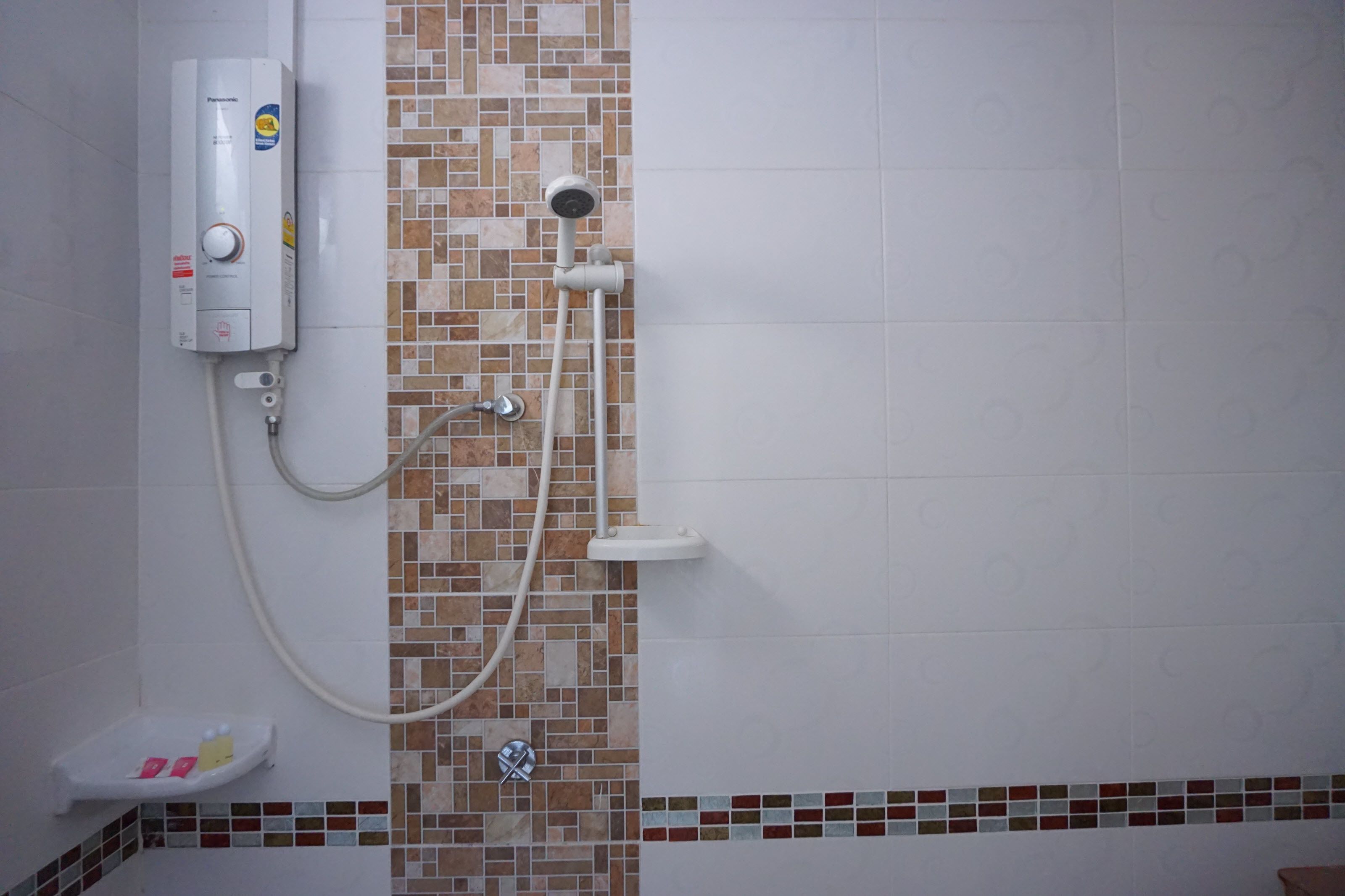 Ein Badezimmer mit weiß gefliester Wand, einer Wand mit Mosaikfliesen, einer Handbrause und einem an der Wand montierten Warmwasserbereiter.
