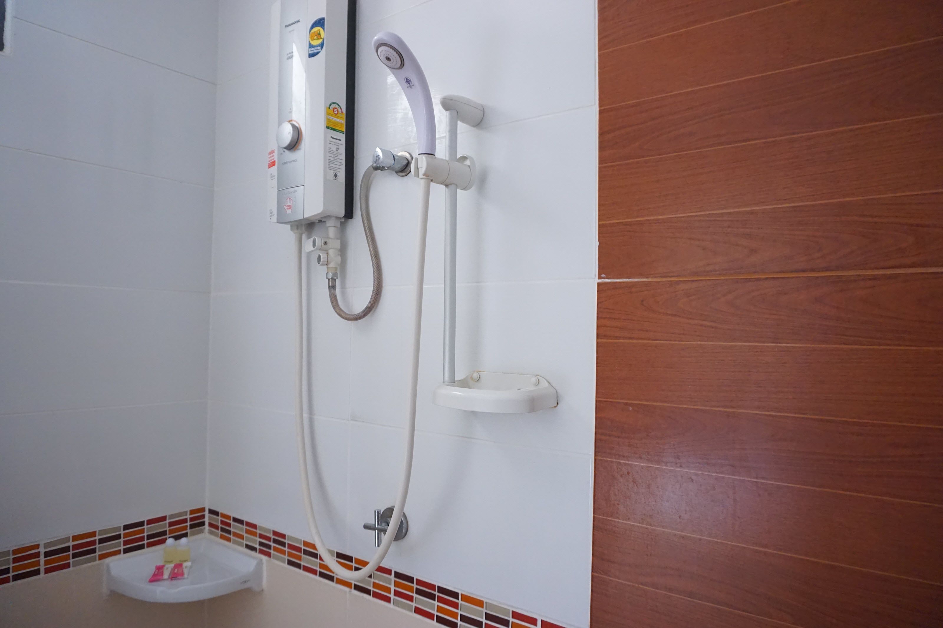 Un baño con pared de azulejos blancos, panel de madera, cabina de ducha y jabonera.