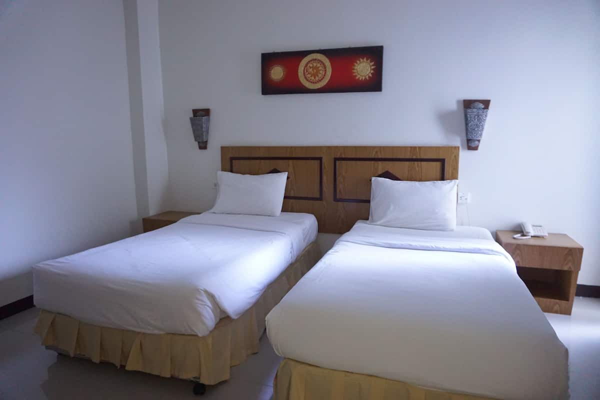 A hotel room with two single beds, a wooden headboard, a wall-mounted artwork, and a bedside table with a phone.