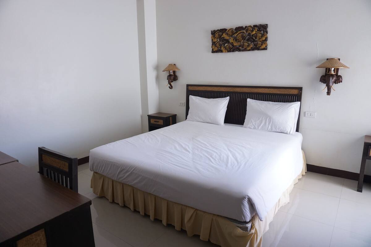 A neatly made bed with white linens, a wooden headboard, and a beige skirt. There are two wall-mounted lamps with animal designs on either side of the bed.