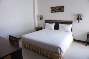 A neatly made bed with white linens, a wooden headboard, and a beige skirt. There are two wall-mounted lamps with animal designs on either side of the bed. - UD Residence (Udon Thani)