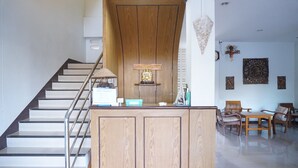 A reception desk with a wooden finish, a staircase with metal railings, and a seating area with wooden furniture. - Chanprasert House (Udon Thani)