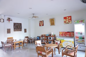 Un comedor con muebles de madera, ventilador de techo, adornos en la pared y un refrigerador con bebidas.