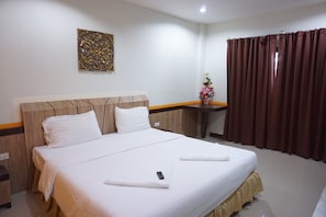 Una habitación de hotel con una cama grande, cabecera de madera, una mesita con un florero y cortinas marrones.