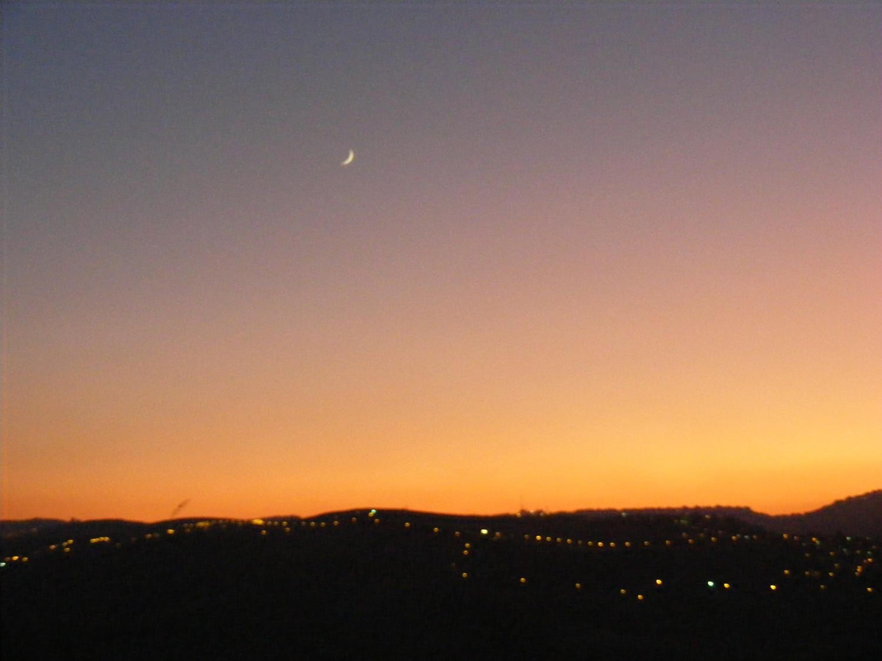 Un paisaje urbano al anochecer con una luna creciente en el cielo.