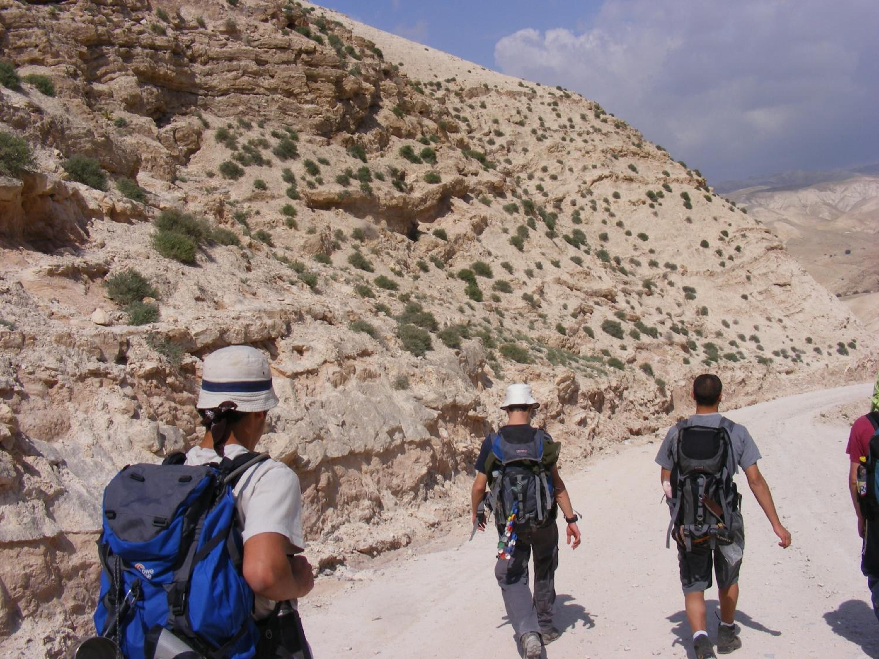 A group of hikers on a rocky trail with sparse vegetation.