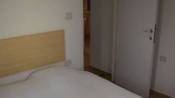 A bedroom with a bed, a wooden headboard, a white door, and a visible bathroom in the background.