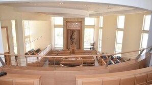 A spacious, high-ceilinged interior with a central staircase, large windows, and a wooden bench area. - Nof Canaan (Nofei Prat)