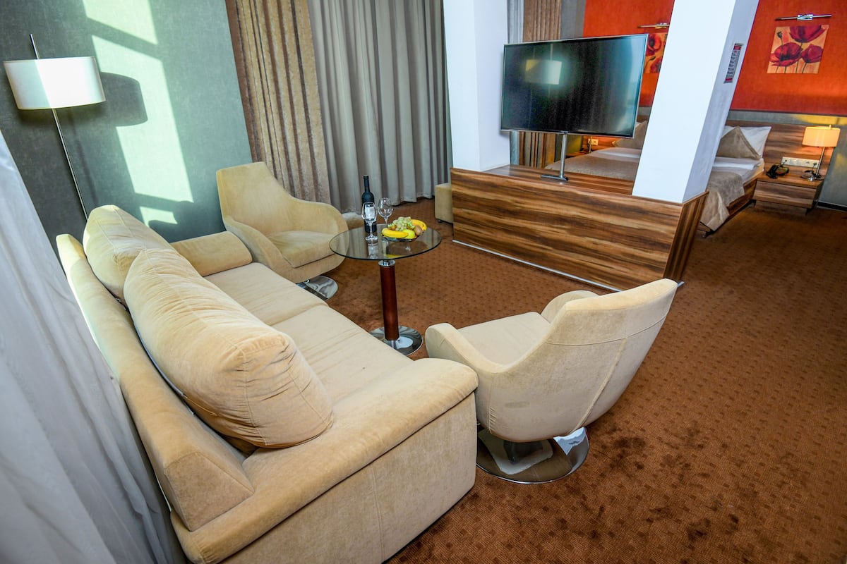 A modern hotel room with a sofa, armchairs, a TV, and a small table with a bottle and glasses.
