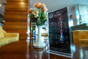 A menu board with a list of hot drinks and beverages, a white vase with flowers, and a wooden table. - Avenue Hotel Baku (Baku)
