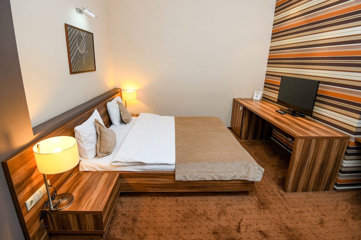 A hotel room with a bed, bedside lamps, a TV, and a striped wall.