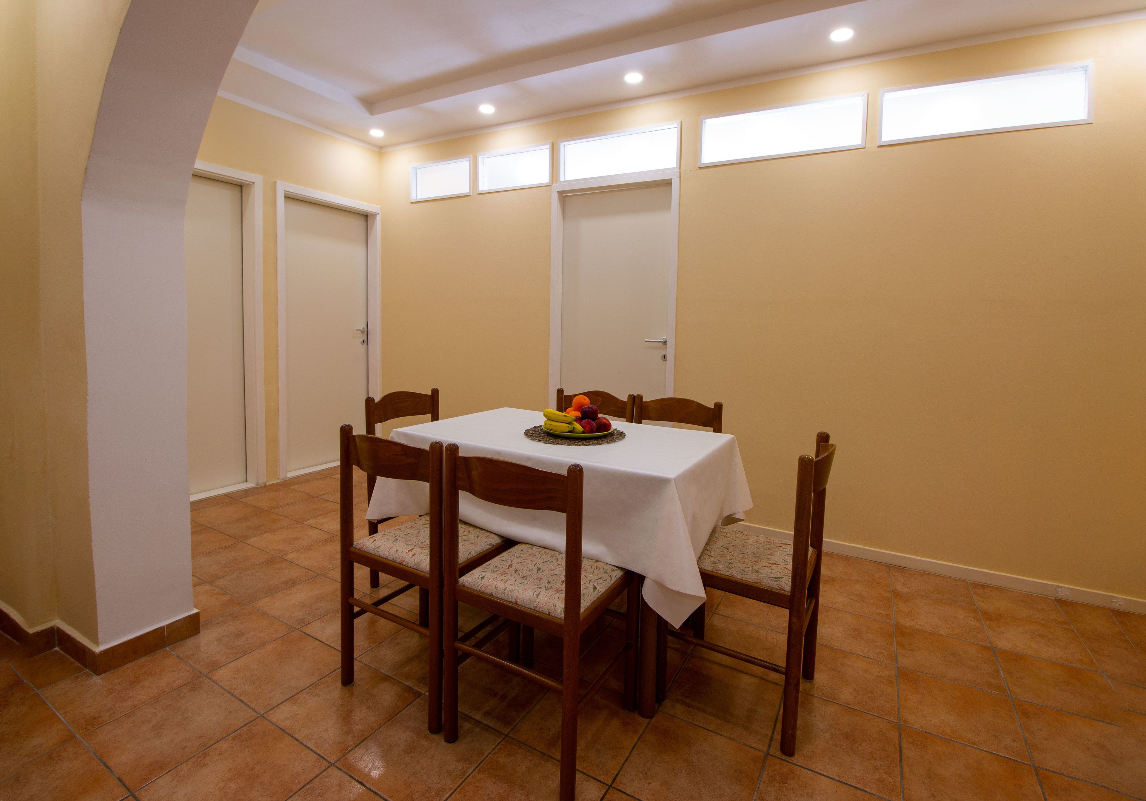 A dining area with a table set for four, surrounded by chairs, and a fruit bowl on the table.