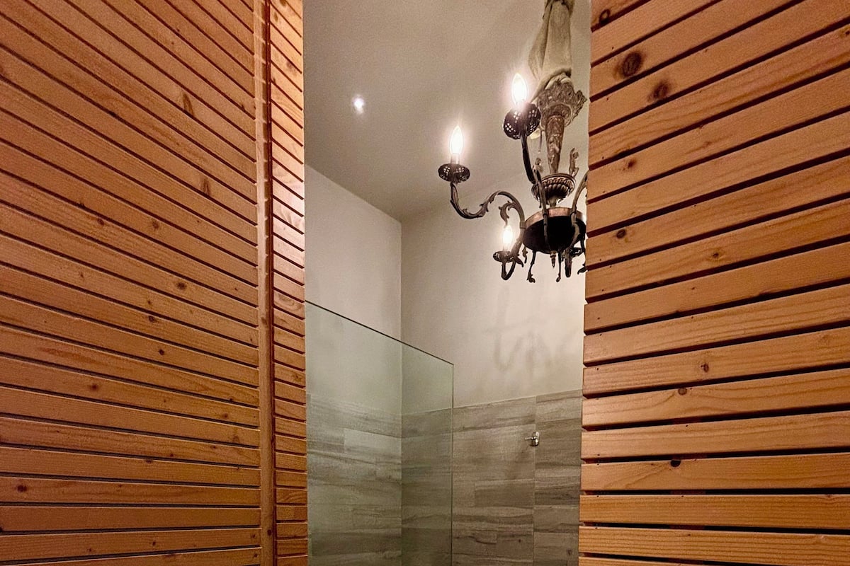 A wooden-paneled bathroom with a glass shower enclosure and a wall-mounted light fixture.