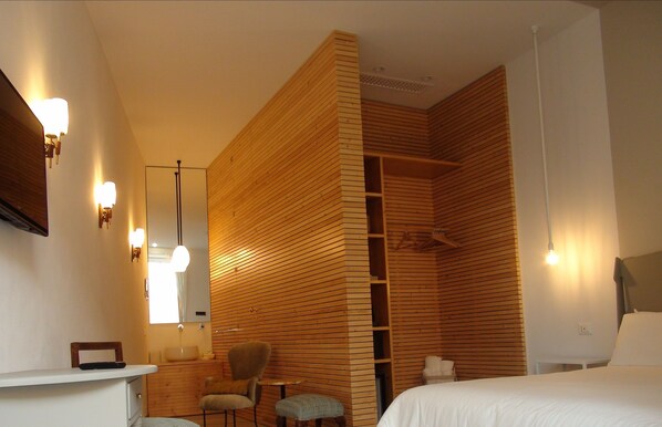 A modern hotel room with a wooden partition, a bed, a chair, a small table, and a mirror. - Room 55 (Noto)