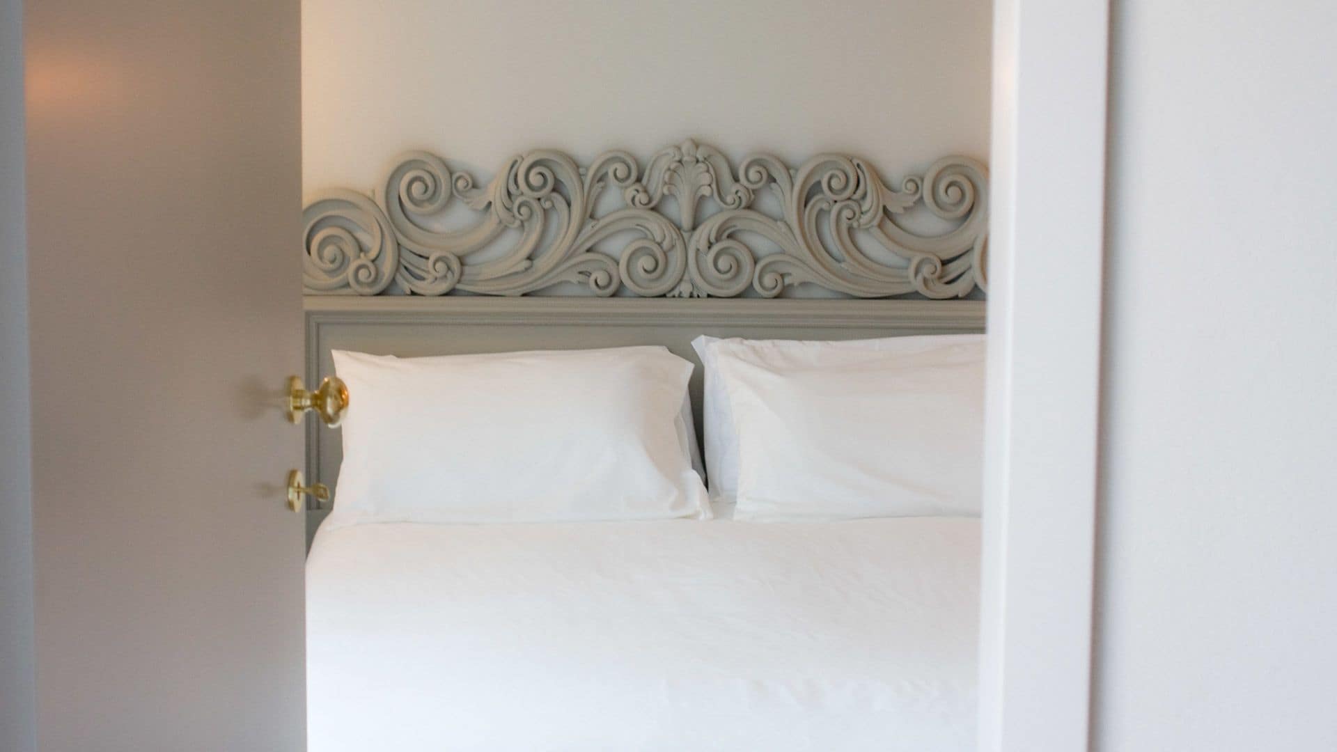 Una cama bien hecha con sábanas blancas y un cabecero decorativo.