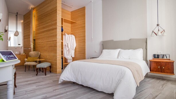 Ein modernes Schlafzimmer mit einem großen Bett, Holzwänden, einer kleinen Sitzecke und einem Schreibtisch mit einem Tablet.