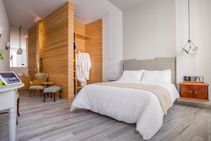 A modern bedroom with a large bed, wooden paneling, a small seating area, and a desk with a tablet. - Room 55 (Noto)