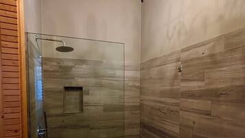 A modern shower with a glass door, wooden panel walls, and a chandelier.