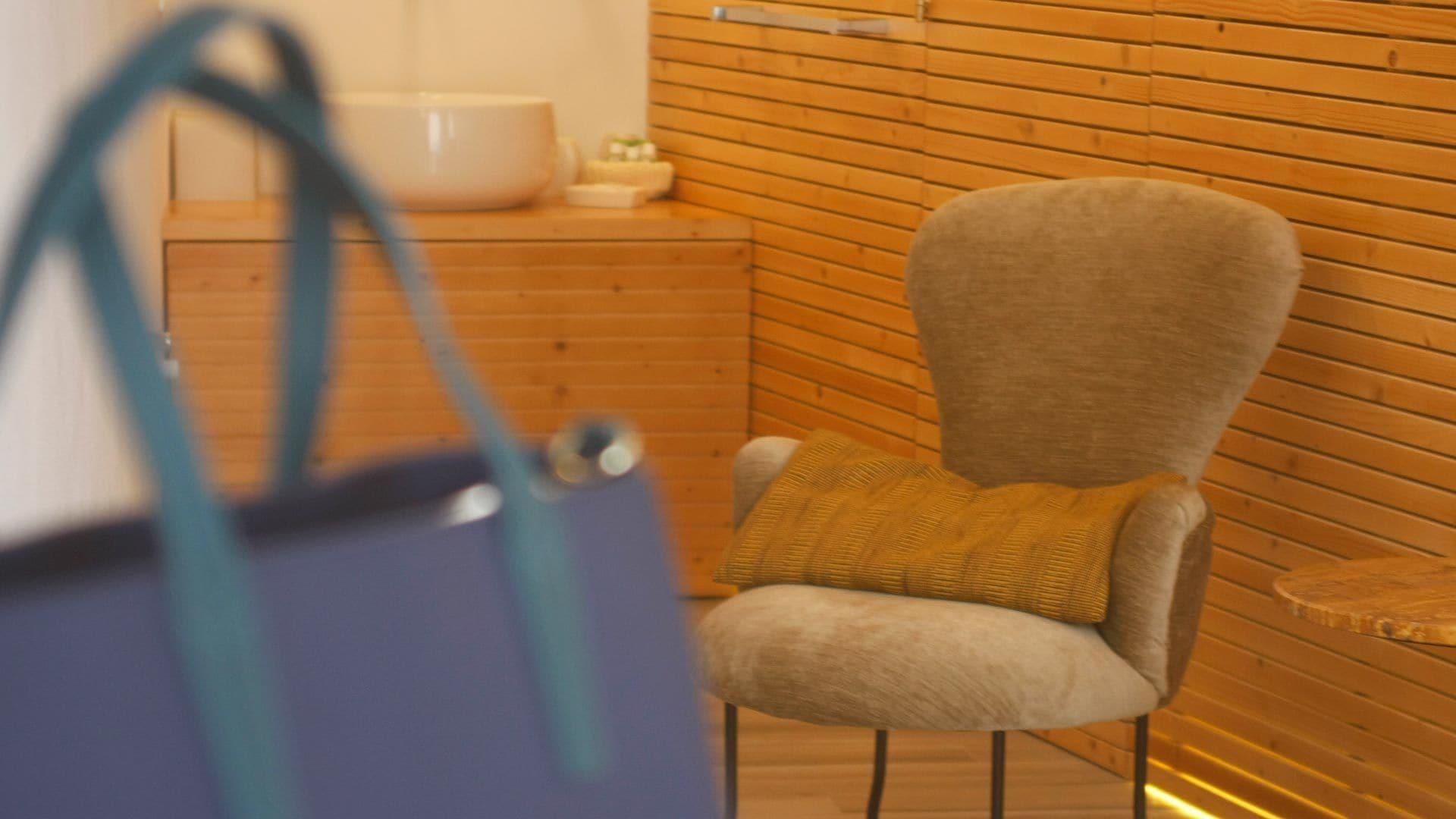 A room with a wooden wall, a chair with a cushion, and a large bag.