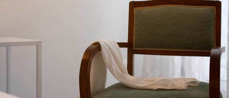 Una silla de madera con asiento y respaldo tapizados en verde, ubicada junto a una mesa blanca.