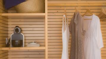 A wooden room with a shelf containing a hairdryer and a basket. There are clothes hanging on a rack.