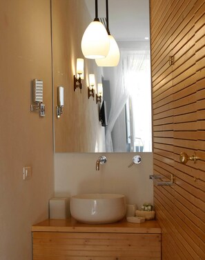 A modern bathroom with a large mirror, a wooden vanity, a white sink, and a pendant light fixture. - Room 55 (Noto)