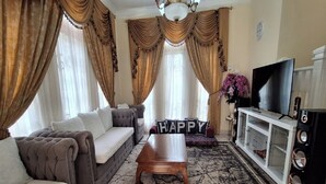 A living room with a sofa, a coffee table, and a TV on a cabinet. - Villa Kota Bunga Anggrek (Cipanas)