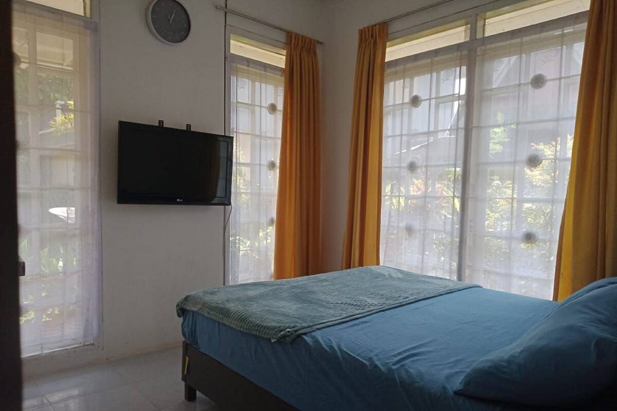 Ein Schlafzimmer mit einem Bett, einem an der Wand montierten Fernseher und Fenstern mit Vorhängen.