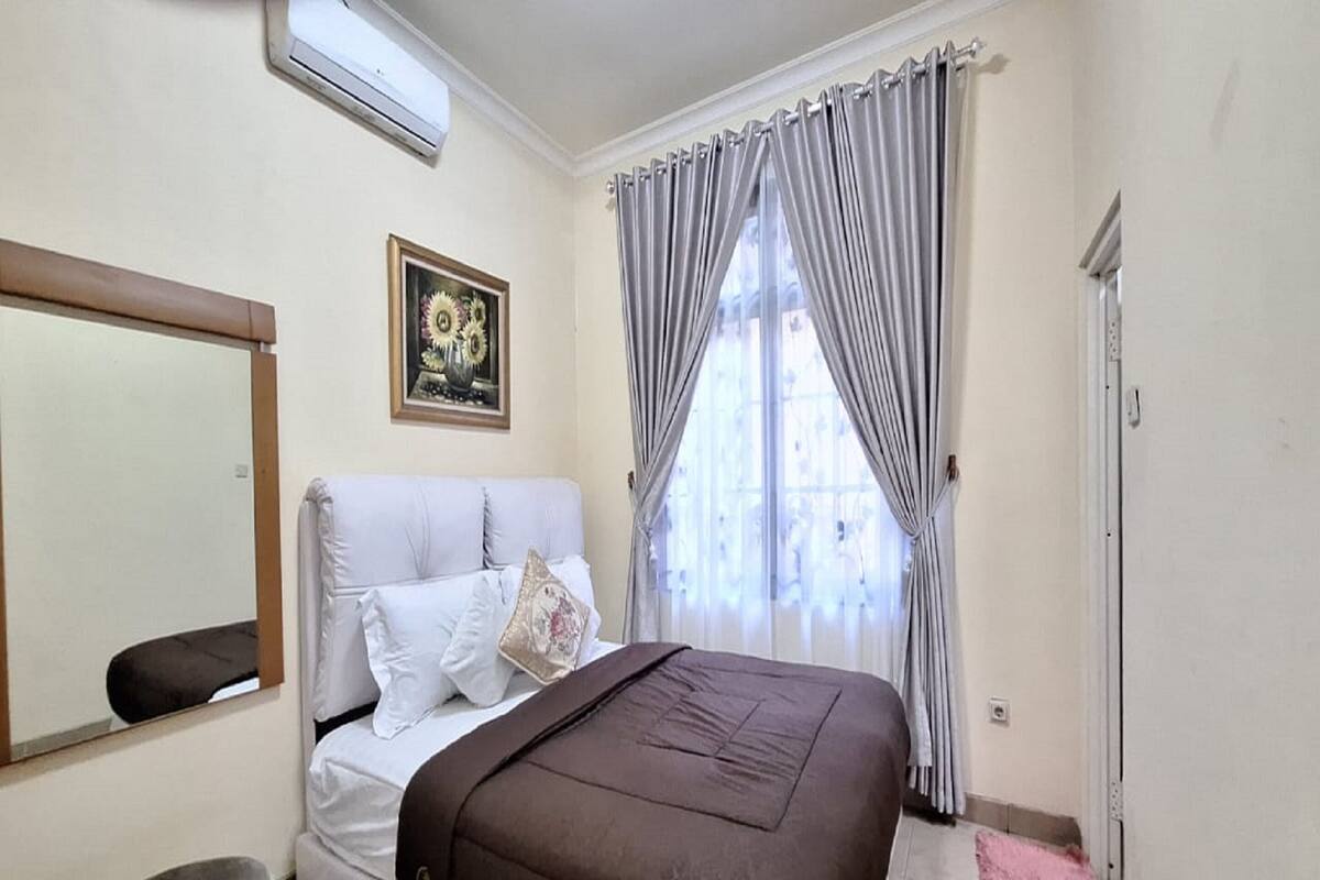 Ein Schlafzimmer mit Bett, Spiegel, Gemälde, Vorhängen und Heizkörper.