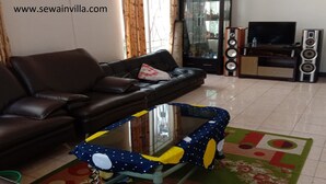 A living room with a sofa, a glass-top coffee table, a television, and speakers. - Villa Kota Bunga Azalea (Cipanas)