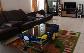 A living room with a sofa, a glass-top coffee table, a television, and speakers. - Villa Kota Bunga Azalea (Cipanas)