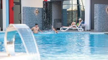A swimming pool area with a water feature, lounge chairs, and a glass door entrance.