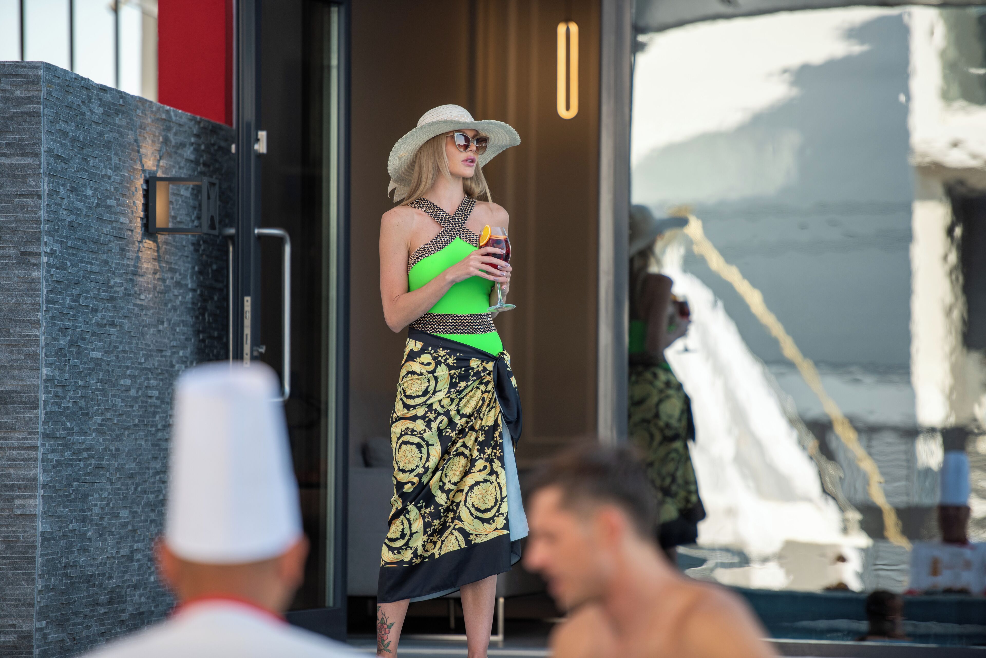 A person standing outside a building with a modern design, wearing a hat and holding a drink.